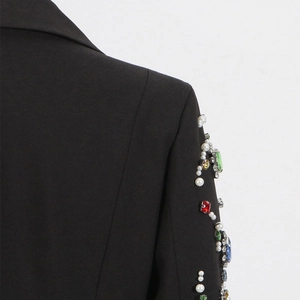 Detailed close-up of handmade faux pearls and colorful crystals on black blazer sleeve