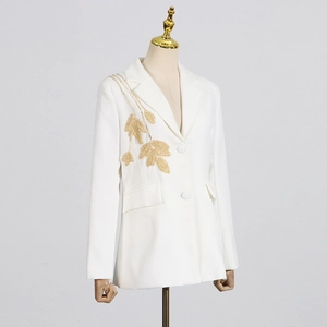 Detailed close-up of golden leaf embroidery on a white elegant blazer jacket
