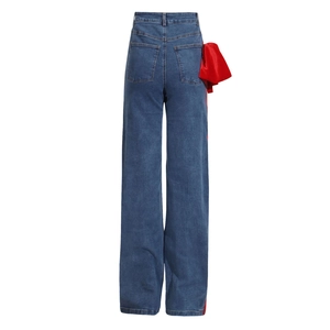 Detail view of high waist denim jeans featuring a large decorative red satin bow on the side