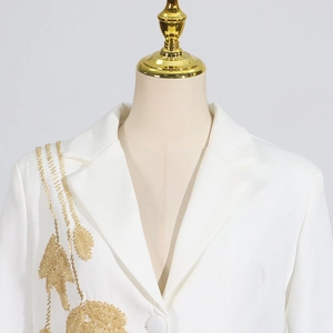 Detailed view of white blazer featuring intricate gold sequins and leaf embroidery patterns