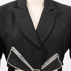 Détail d'un blazer noir avec un grand nœud orné de cristaux et de perles brillantes