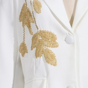 Detailed view of white blazer with gold sequin and bead embroidery in a leaf pattern