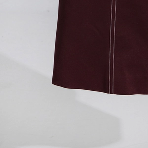 Detailaufnahme der weißen Doppelnaht am Saum eines weinroten Trenchcoats für Damen