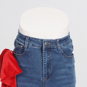 Detail of high waist denim jeans featuring a large red velvet bow on the side waist