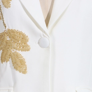 Detail of white blazer featuring intricate gold leaf beadwork and a fabric-covered button