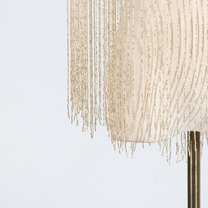Close-up of intricate gold beaded fringe tassels on a stylish beige women's outerwear shawl
