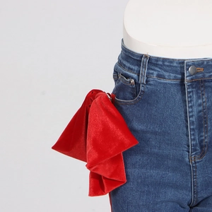 Detail of a red velvet bow accessory attached to the side pocket of blue denim jeans