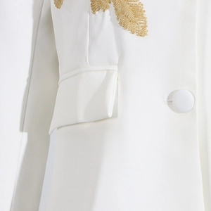Detailed view of white blazer featuring golden leaf bead embroidery and fabric button