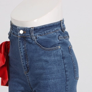 Detail of high waist denim jeans featuring a decorative red satin bow and metal button