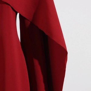 Détail macro du tissu tissé rouge montrant les finitions effilochées élégantes du manteau