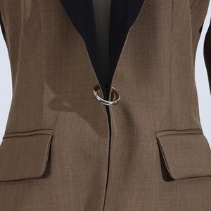 Detail of brown blazer featuring black lapel contrast and silver circular metal buckle