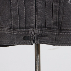 Vue macro de l'ourlet d'une veste en jean gris foncé avec plis et détails en strass