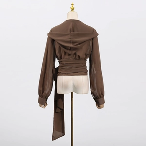 Detail of hooded brown blouse featuring a waist-tie design and long sleeves with button cuffs