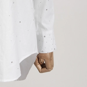 Macro detail of white shirt sleeve featuring sparkling rhinestones on smooth fabric