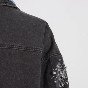 Détail de motifs floraux en strass cousus main sur la manche d'une veste en jean gris foncé