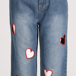 Detailed close-up of heart-shaped hollow embroidery on light blue denim jeans