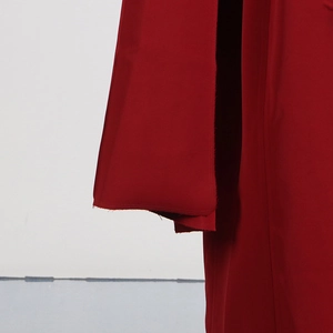 Détail de l'ourlet à bord franc sur un trench-coat rouge au fini tissu premium