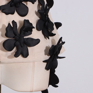 Close-up of 3D black flower appliqués on sheer beige mesh top on white mannequin