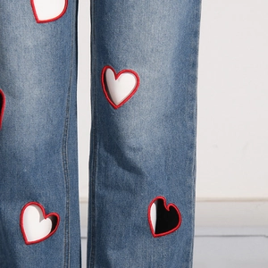 Detailed macro view of heart-shaped cutouts with red embroidery on blue denim jeans