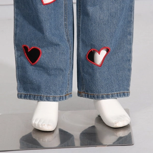 Detailed view of blue denim hem featuring heart-shaped cutout and red embroidery