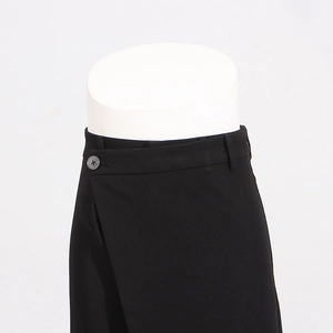 Detail of high-waist trousers featuring asymmetric waistline and button closure