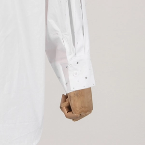 Close-up of white shirt sleeve featuring sparkling rhinestones and button cuff detail