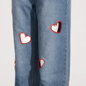 Detail of red heart embroidery and textured blue denim fabric on high waist straight jeans