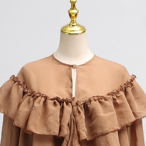 Close-up of brown ruffled shirt with buttoned round neck and mesh splice details