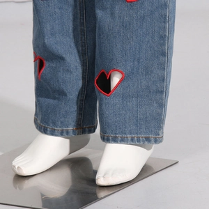 Detail of blue denim pants featuring a red heart embroidery and high-quality stitching