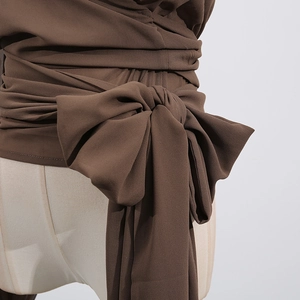 Detail of the brown textured chiffon top featuring cross-wrap waist straps and a large bow
