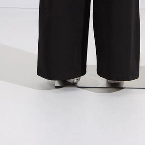 Detail view of black wide-leg trousers featuring a sharp drape and neat hemline stitching