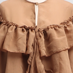 Detail of ruffle layers and covered button on brown long-sleeve blouse for women