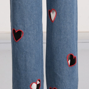 Close-up of denim jeans featuring heart-shaped cutouts with red embroidered edges