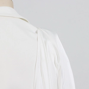Detail view of the gathered shoulder seam and draped white fabric texture of the blouse