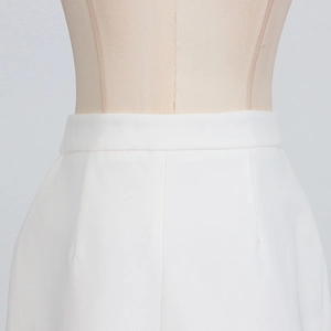 Detailed view of high-waist white skirt with pleated details and woven fabric texture