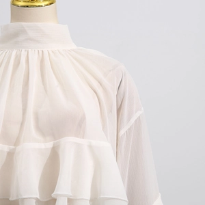 Detail of white chiffon blouse showing ruffled layers and elegant stand collar design