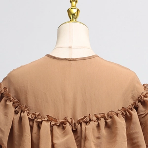 Detail of tan ruffled blouse featuring lightweight textured fabric and round neckline
