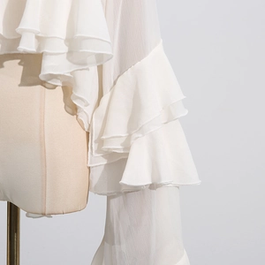 Close-up of white chiffon blouse showing layered ruffle cuffs and sheer mesh texture