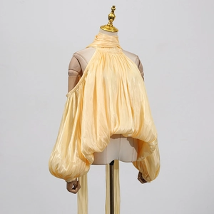 Detail view of the yellow halter neck shirt showing shiny fabric and pleated lantern sleeves
