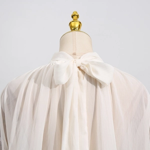 Detail of elegant cream chiffon blouse featuring a large self-tie bow on the back neck