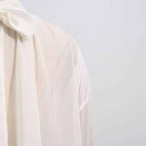 Detailed view of elegant cream chiffon blouse with pleated texture and bow tie neckline