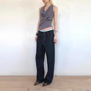 Detail of grey draped sleeveless top with silver side buckle and multi-button jeans