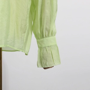 Detail of light green shirt showing flared ruffled cuffs and pleated fabric texture