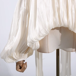 Close-up of pleated cream satin fabric showing elegant texture and glossy finish