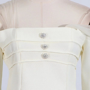 Close-up of cream tweed top featuring rhinestone star buttons and sheer mesh panels