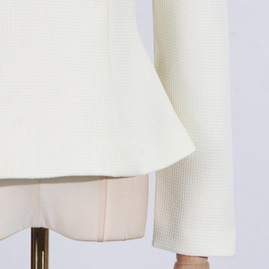 Detailed close-up of cream textured tweed fabric with elegant peplum waist and sleeve design