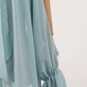 Detail of light blue chiffon shirt featuring ruched cuffs and elegant ribbon accents