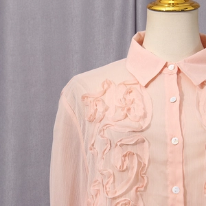 Detail of pink chiffon blouse showing layered ruffle chest design and pearl buttons