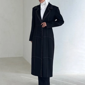 Detail of a black long coat with white contrast stitching and tailored notched lapels