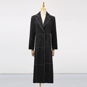 Detail of long black trench coat featuring white contrast stitching and tailored lapels